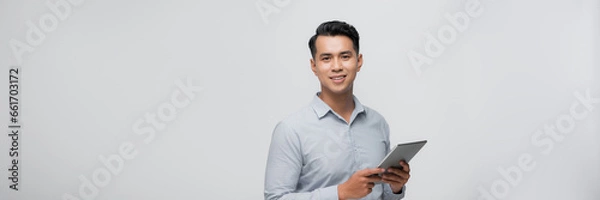 Fototapeta A portrait of a young asian man holding a digital touch screen tablet computer on white background.