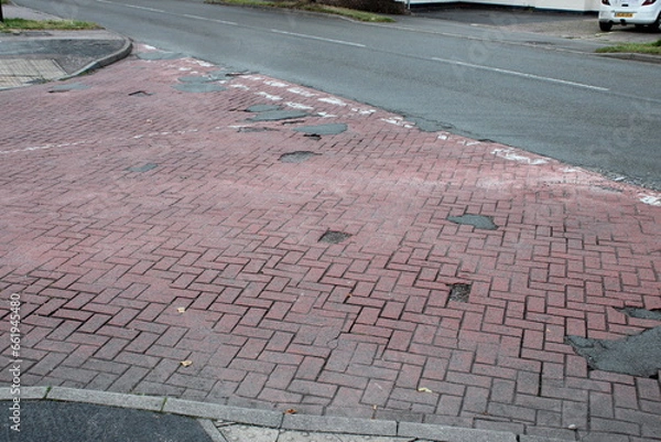 Fototapeta Patchy UK junction paved with red bricks and various potholes filled with tarmac