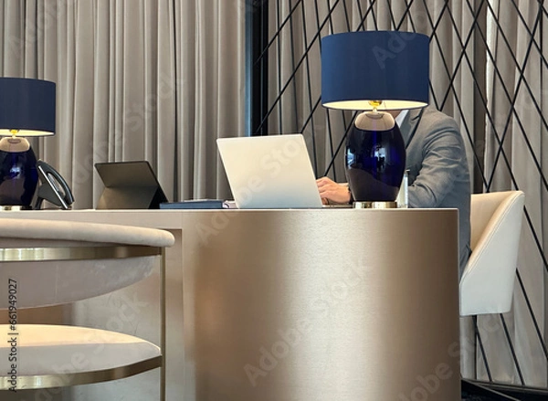 Fototapeta Man in suit working on laptop at the table in lounge, reception, lobby, hall, foyer or office space.