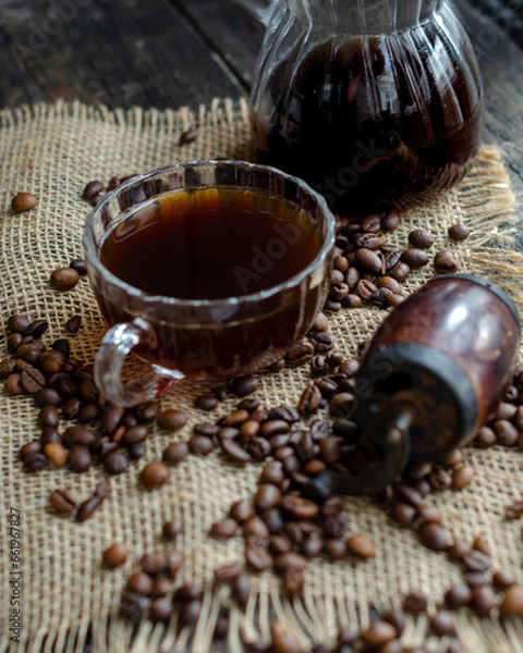 Fototapeta Coffee in a transparent cup, coffee beans, a transparent glass cezve and a manual coffee maker on an organic fabric on the table, morning, breakfast, photo in a dark key