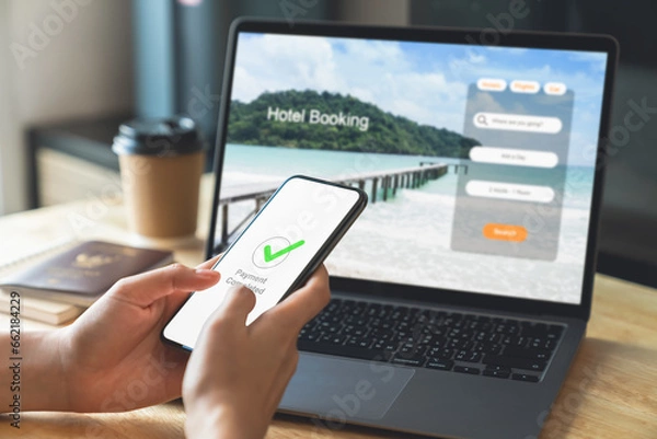 Fototapeta Hand using laptop and booking hotel on website for vacation after a long work and payment completed message on mobile, Summer holiday concept.