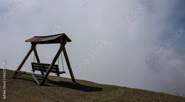 Fototapeta Wooden swing on the mountainside against the backdrop of a dramatic cloudy sky and a space to copy