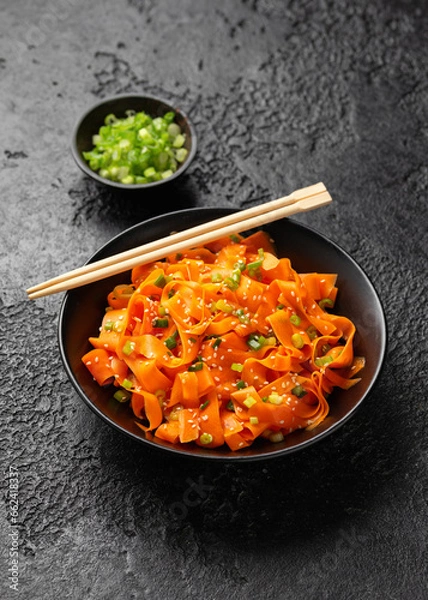 Fototapeta Asian carrot salad with spices and herbs in black bowl.