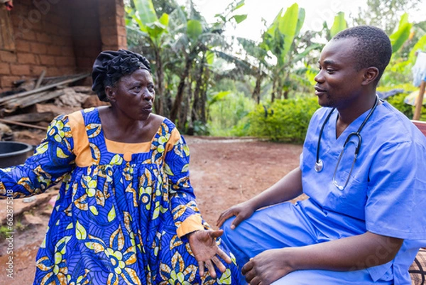 Obraz A doctor talks to his elderly patient during a home visit in an African village