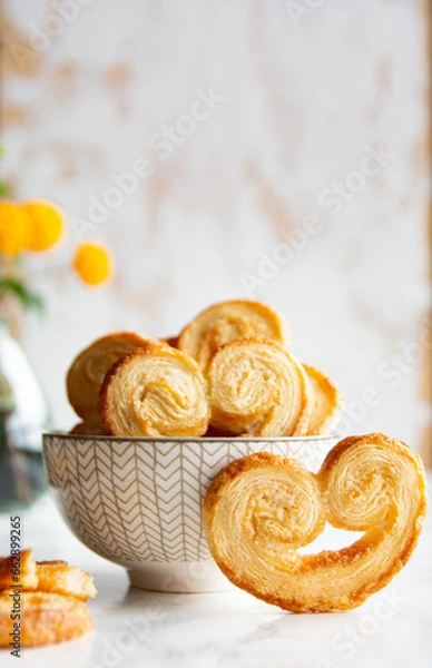 Obraz Puff pastry palmiers in a bowl on a white marble table. Homemade bakery for breakfast. Vertical picture.
