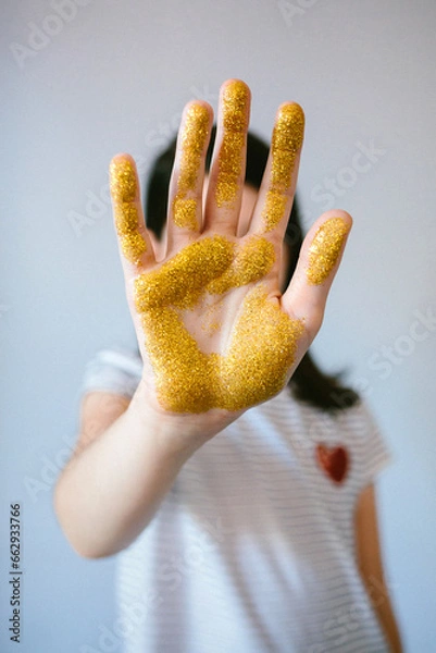 Fototapeta Unrecognizable young girl showing her palm hand covered of golden glitter while doing stop sign. Concept of harmful microplastics composition to humans and environment. Selective focus on hand.