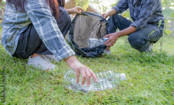 Fototapeta Hand holding plastic bottles waste, Couple picking up trash putting to the black garbage bag at Sunflower Park on Environmental Earth day