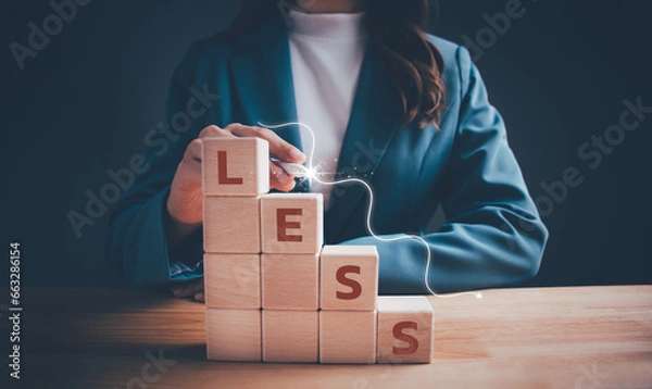 Fototapeta Businesswoman with the word "LESS" on descending step stairs of wooden blocks cubes. Spending less, cutting down expenses, economic crisis, cut costs business, more saving business concept.
