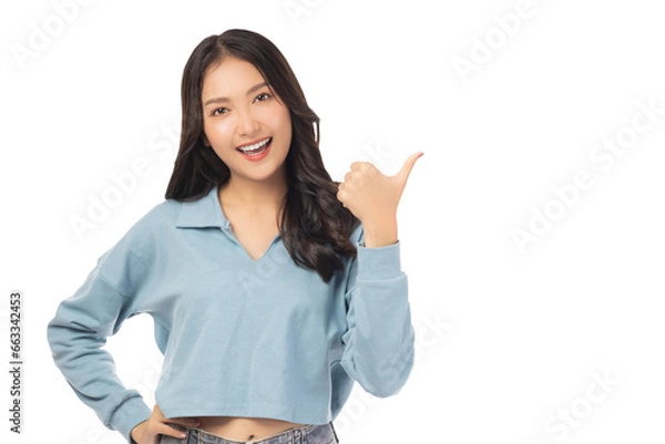 Fototapeta Beautiful young Asian woman pointing up to copy space and looking at camera with smile face and happy Pretty girl act like a satisfied product, use for advertising with isolated on white background