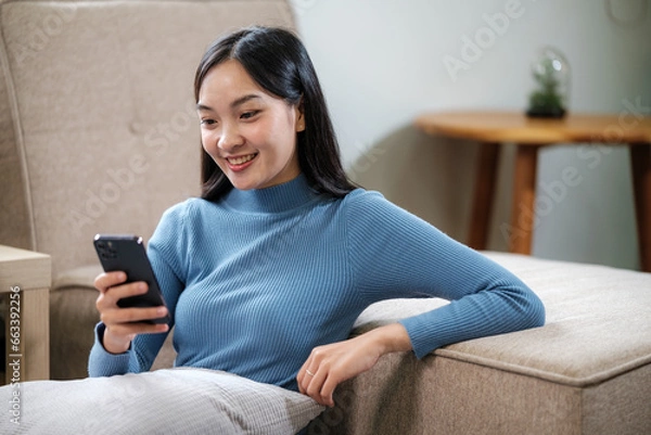 Fototapeta Smiling woman holding smartphone and banking credit card, involved in online mobile shopping at home, happy female shopper purchasing goods or services in internet store.
