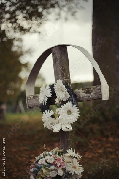 Obraz Old wooden cross headstone with flowers on traditional European cemetery. Close up of aged cross head stone on grave yard in the evening. Autumn scene. Single cross gravestone with floral decoration