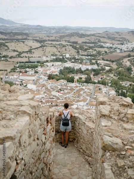 Obraz Traveler tourist woman with backpack looking at an Andalusian town from the top of the ruins of a medieval castle.