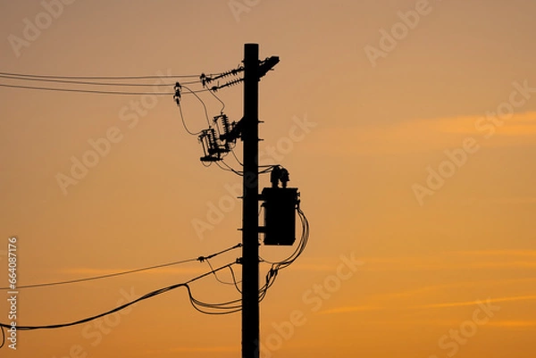 Fototapeta Power pole silhouette with resistors and transformers on a power grid under a sunset sky in Alberta Canada.