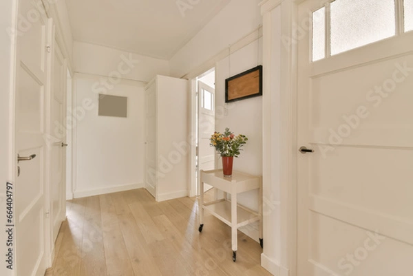 Fototapeta a hallway with white walls and wood flooring in an empty house, showing the entrance way to another room