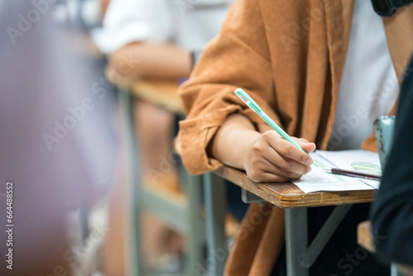 Fototapeta Selective focus high school or university students concentrate writing on paper answer sheet for final exam in the classroom