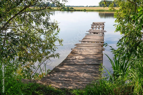 Fototapeta A wooden bridge made of logs and partially rotten boards. Being careful is dangerous. Water, lake, bush. Shore.