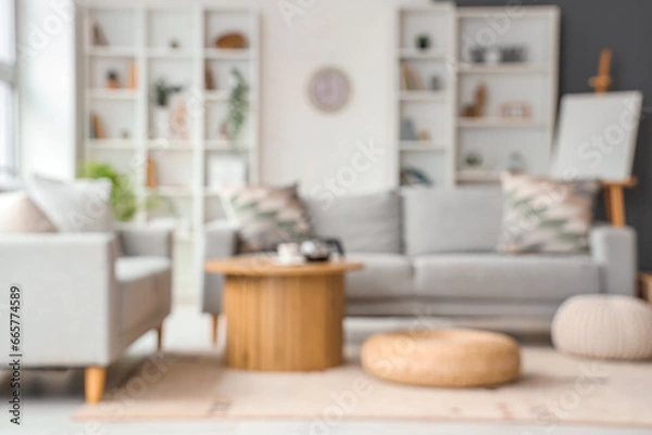 Fototapeta Blurred view of living room with sofas, table and poufs