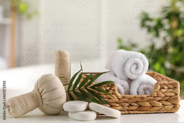 Obraz Spa composition. Towels, stones, herbal bags and palm leaves on white table indoors