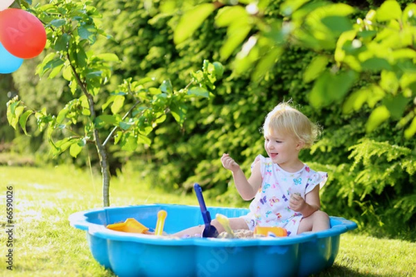 Fototapeta Happy little girl playing in sandbox in the garden