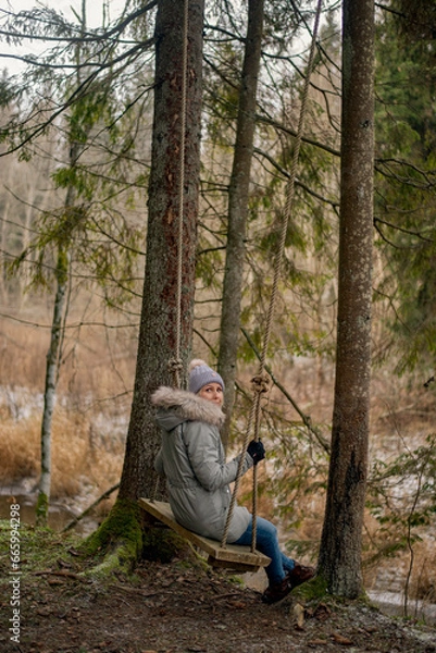 Obraz woman sitting on swings in the middle of the forest in cold winter time, warm clothes 