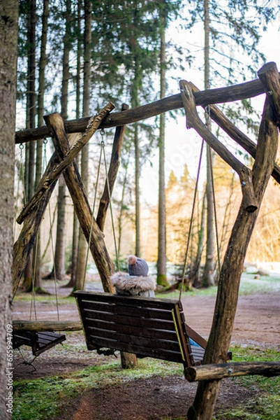 Obraz woman sitting on swings in the middle of the forest in cold winter time, warm clothes 