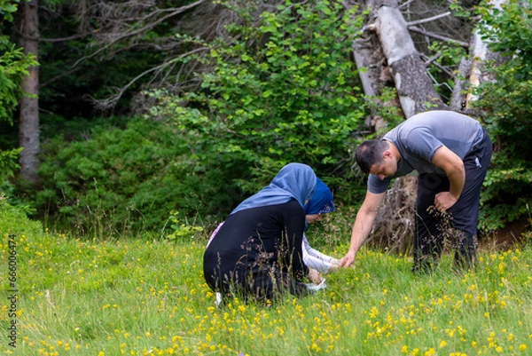 Fototapeta Muslim youth enjoying time in nature while picking blueberries. Happy brother and sisters collecting bilberries in forest. Agricultural concept