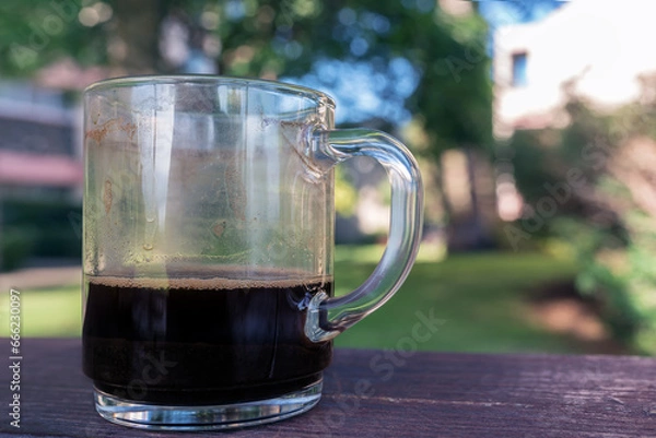 Fototapeta a glass mug with finished coffee in it , on a wooden table in the park