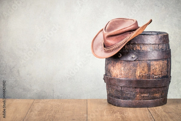 Obraz Wild West old retro leather cowboy hat and aged antique oak barrel. Vintage style filtered photo
