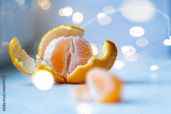 Obraz Juicy, fresh, peeled tangerine and garland lights in the background. Bokeh of garlands in the background, and in the foreground is a peeled tangerine.
