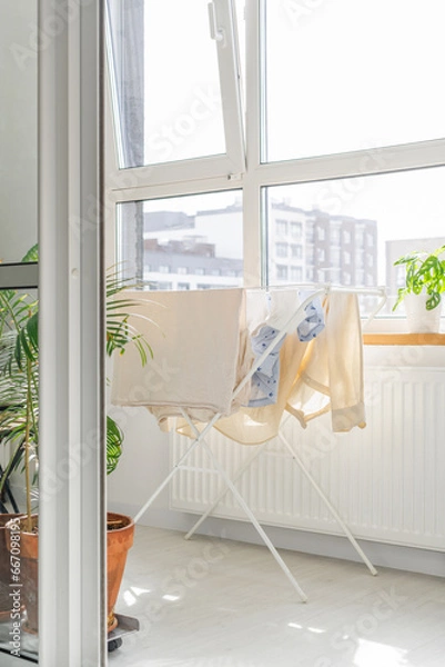 Fototapeta beige clothes to dry on a white clothes dryer on a bright Scandinavian balcony on a sunny day among greenery