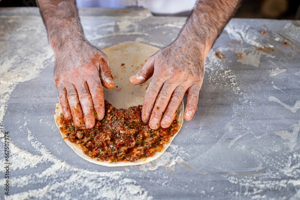 Fototapeta Preparing and baking lahmacun . Hands of a male making meat pizza. 