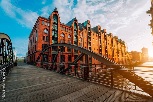 Fototapeta Arch bridge over canals in the Speicherstadt of Hamburg. Warm evening sun light on red brick building