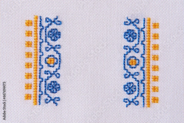Fototapeta Element of Handmade Embroidery on White Linen by blue and yellow Cotton Threads. Craft Design