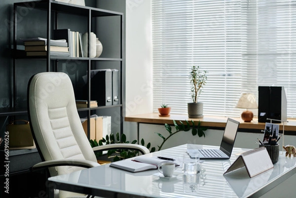 Fototapeta Comfortable armchair standing next to workplace of chief executive officer of modern business organization with laptop, calendar and other stuff