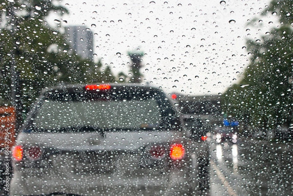 Fototapeta Raindrops cling to the windshield of a car while driving on the road.