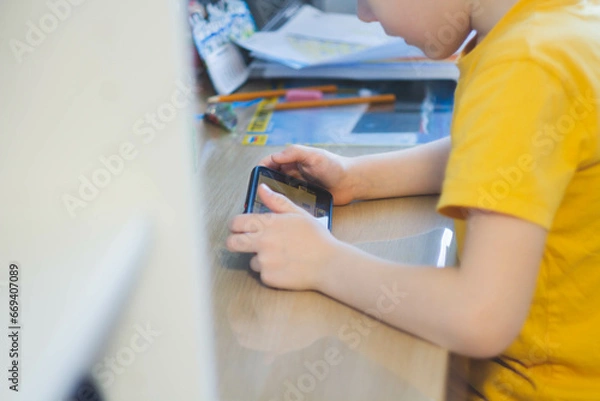 Fototapeta Phone in hands of child. Little boy playing mobile games on smartphone. Hand closeup.