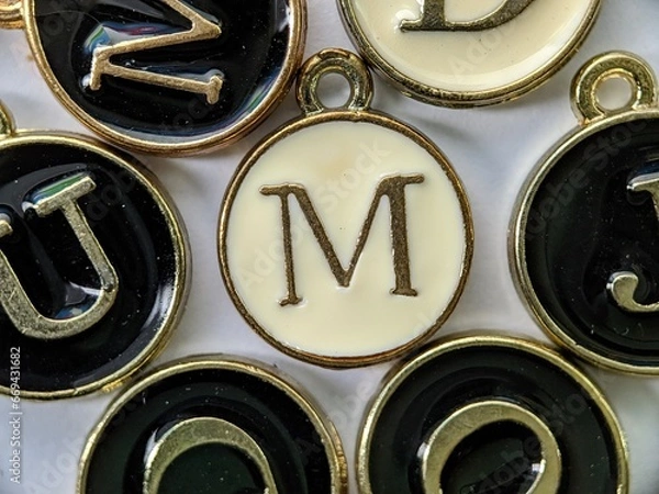 Fototapeta white and gold initial 'M' pendant in the middle of several letters