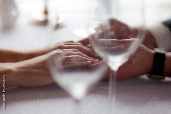 Fototapeta Close-up of Hands Resting on a Table with Wine Glasses, Captured in Soft Focus