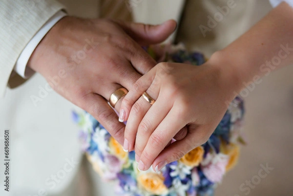 Fototapeta Close-up of newlyweds' hands, with an emphasis on wedding rings, against a background of a flowers.