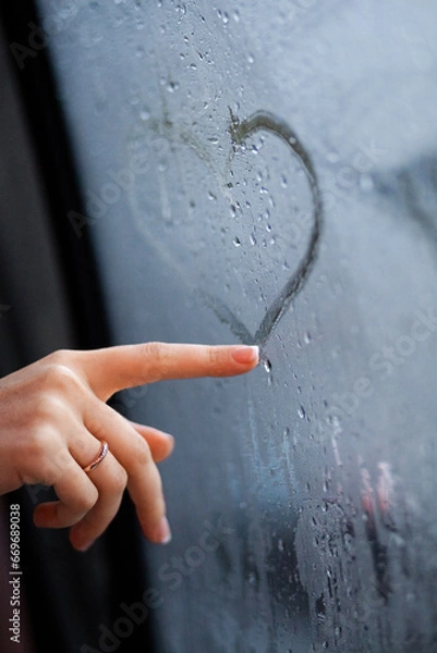 Fototapeta A woman's hand draws the shape of a heart on the fogged window.