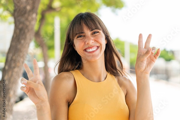 Obraz Young woman at outdoors showing victory sign with both hands