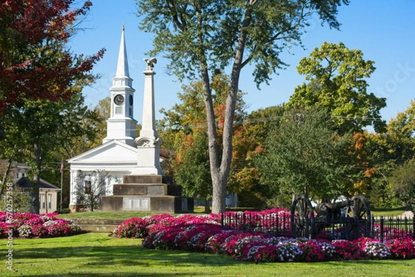 Fototapeta Colorful beds of flowers cluster on the town square in Twinsburg, Ohio, with in front of the civil war monument and a historic old church.