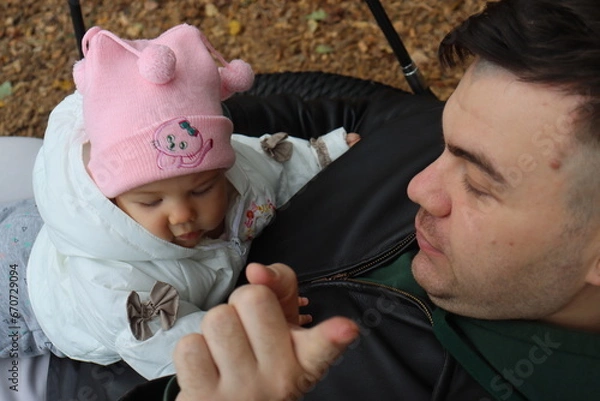 Obraz dad holds a little girl in his arms and rides on a swing in the park in autumn