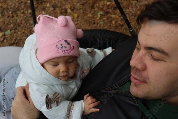 Obraz dad holds a little girl in his arms and rides on a swing in the park in autumn
