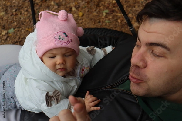 Obraz dad holds a little girl in his arms and rides on a swing in the park in autumn