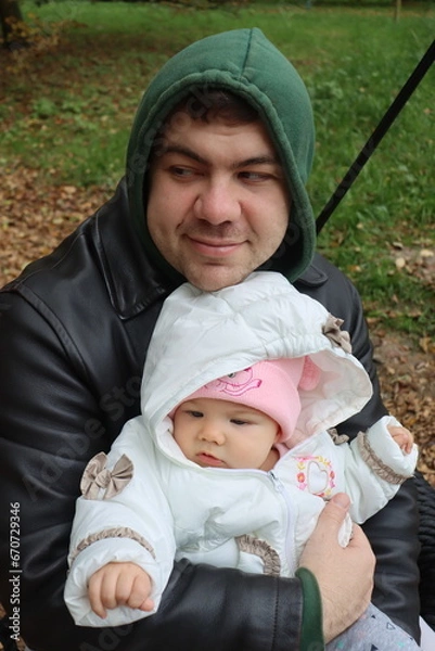 Obraz dad holds a little girl in his arms and rides on a swing in the park in autumn