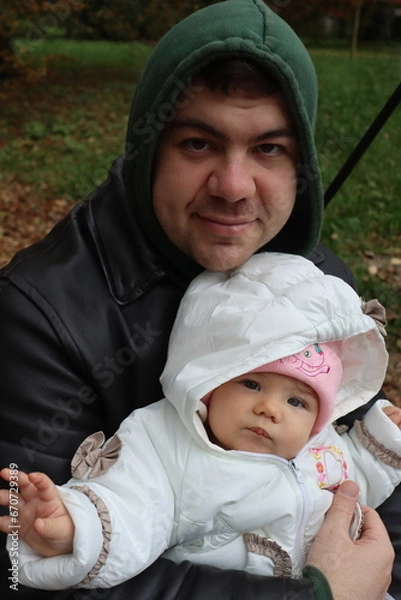 Obraz dad holds a little girl in his arms and rides on a swing in the park in autumn