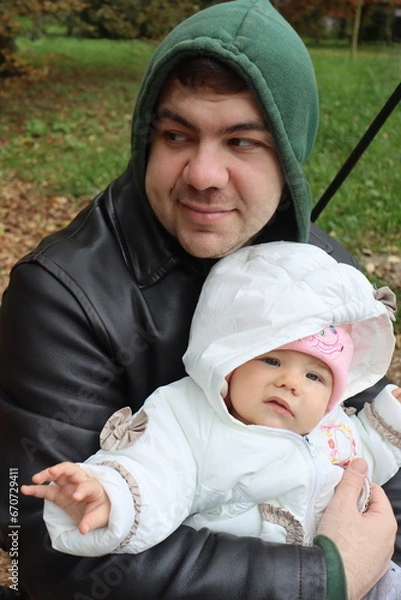 Obraz dad holds a little girl in his arms and rides on a swing in the park in autumn