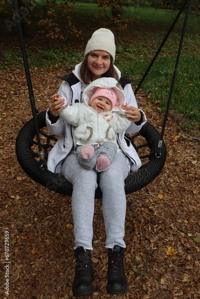 Obraz mother holds a little girl in her arms and rides on a swing in the park in autumn