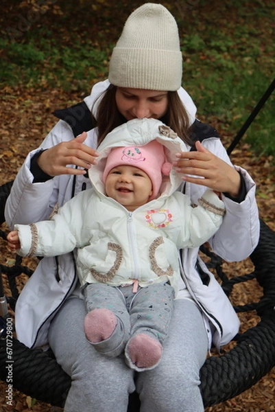 Obraz mother holds a little girl in her arms and rides on a swing in the park in autumn